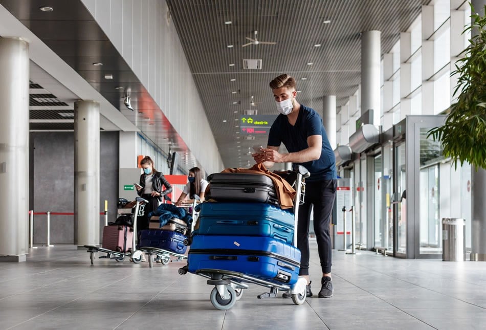 Passenger standing inside airport entrance with luggage on baggage cart